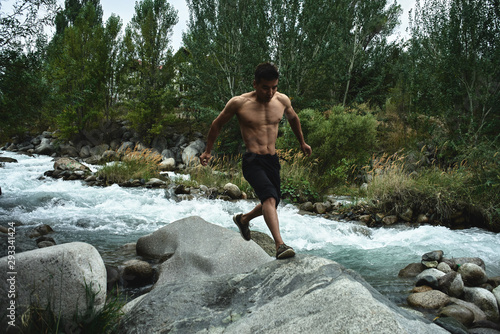 Kazakh muscular athlete man trains and exercises by the river in nature. Asian handsome does extreme fitness workout outdoors