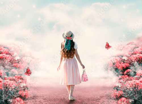 Young lady woman in romantic dress, hat with bag in retro style walking along summer rose field path and flying butterfly. Idyllic tranquil fantasy scene. Travel across fairy tale hills