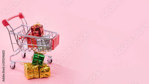 Annual sale, Christmas shopping season concept - mini red shop cart trolley full of gift box isolated on pale pink background, copy space, close up