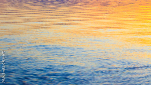 Clear water texture in blue and orange. Background of the ocean and the sea backlit by the sun. Soft waves. Natural water