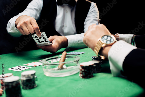 cropped view of man near croupier with playing cards isolated on black