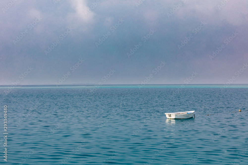 Lonely boat on calm sea on cloudy morning. Sea horizon with copy space