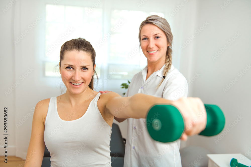 A Modern rehabilitation physiotherapist at work with client. Working on shoulder with dumbell A Modern rehabilitation physiotherapist at work with client. Working on shoulder with dumbell