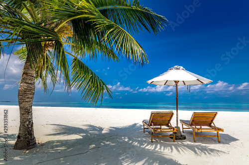 Luxury summer beach view. Chaise lounge concept with two beach chairs and umbrella on white sand with palm tree. Perfect beach landscape for vacation or holiday template. © icemanphotos
