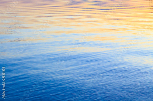 Clear water texture in blue and orange. Background of the ocean and the sea backlit by the sun. Soft waves. Natural water