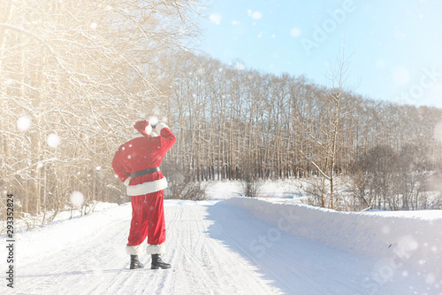 Santa Claus comes with gifts from the outdoor. Santa in a red suit with a beard and wearing glasses is walking along the road to Christmas. Father Christmas brings gifts to children.