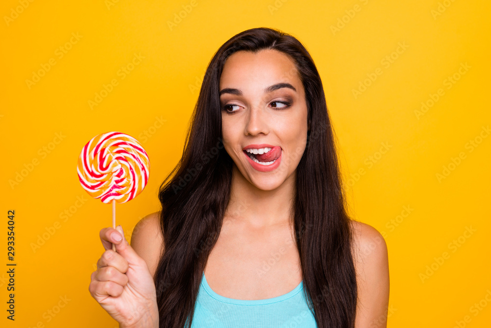 Photo of funny flirty cute nice charming youngster looking over her candy licking her upper lip waiting for lollipop to be eaten wearing teal tank-top isolated over vivid color background