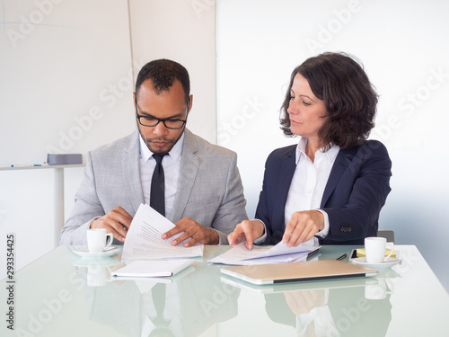 Professional business people signing contract. Serious multiethnic businessman and businesswoman sitting at table and working with papers in office. Paperwork concept