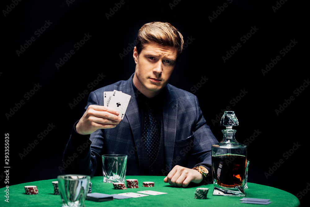 selective focus of handsome man holding playing cards near poker chips and alcohol drink isolated on black selective focus of handsome man holding playing cards near poker chips and alcohol drink isolated on black