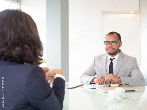 Cheerful businessman talking with colleague. Young African American businessman in eyeglasses sitting at table with female colleague during business meeting. Job interview concept