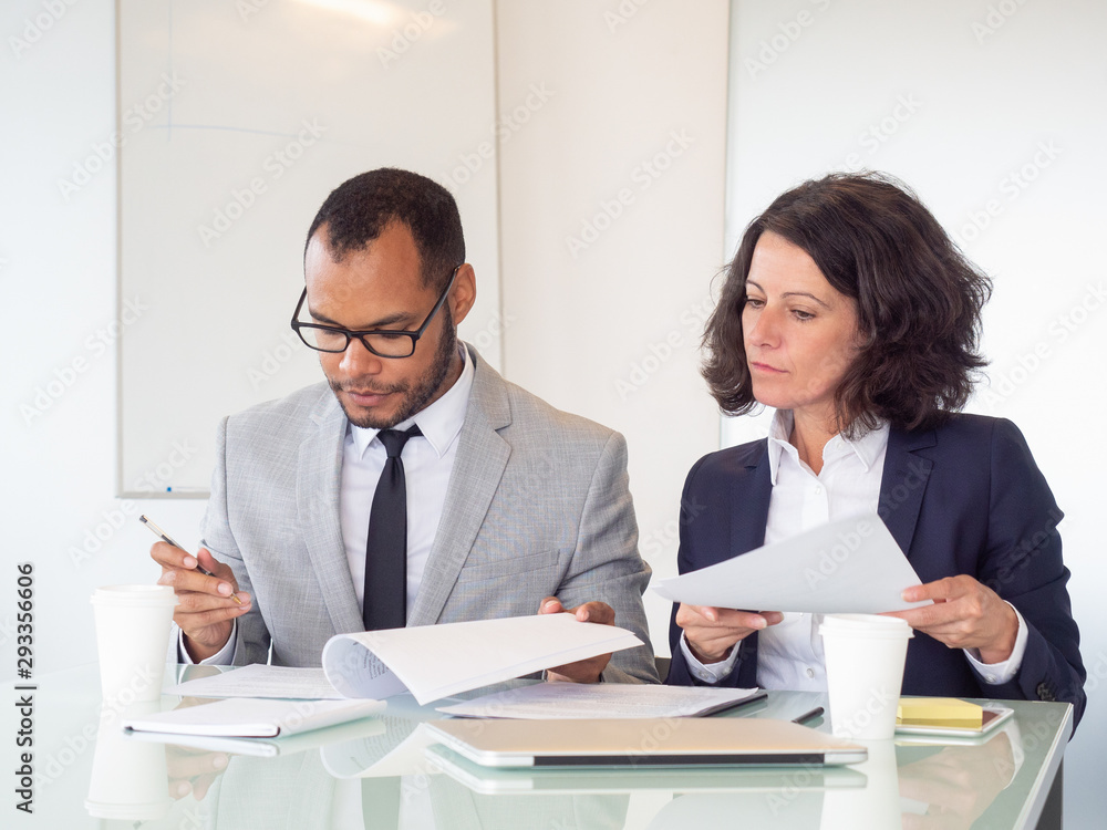 Business people signing contract. Serious multiethnic businessman and businesswoman sitting at table and working with papers in office. Paperwork concept Business people signing contract. Serious multiethnic businessman and businesswoman sitting at table and working with papers in office. Paperwork concept
