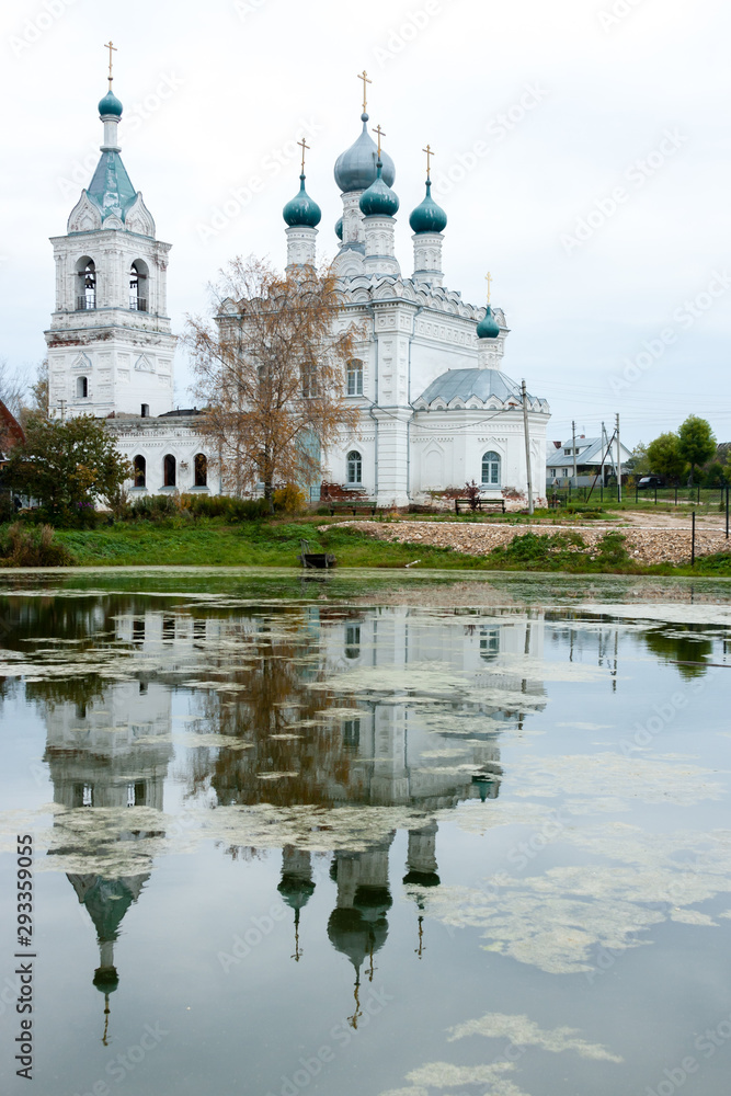 Autumn day in traditional Russian village. Autumnal sad landscape with church reflections on the lake