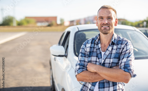 An attractive young man stands near a white car.