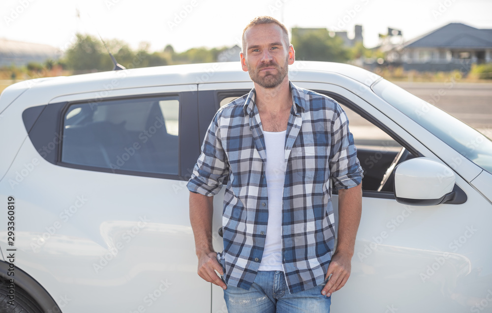 An attractive young man stands near a white car. An attractive young man stands near a white car.