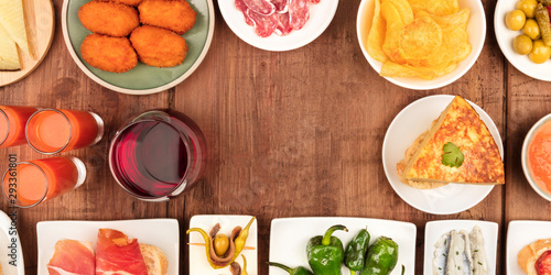 A panorama of Spanish tapas, a variety of snacks, top shot. Gazpacho, tortilla, and wine, shot from above on a dark rustic wooden background with a place for text