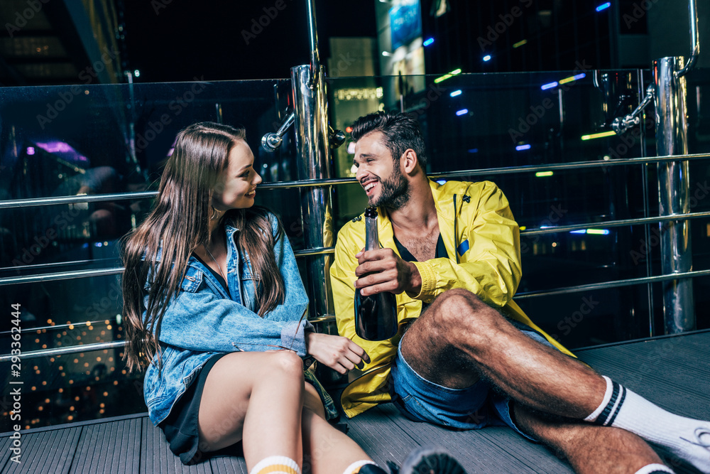 handsome boyfriend with bottle and attractive girlfriend smiling and talking in night city