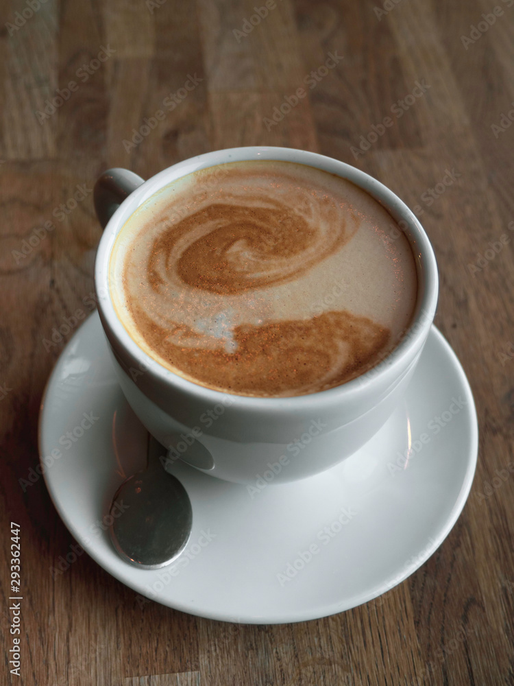 A beautiful cup of cappuccino with latte art in the wooden background. Minimal composition. Copy space for your text. A beautiful cup of cappuccino with latte art in the wooden background. Minimal composition. Copy space for your text.