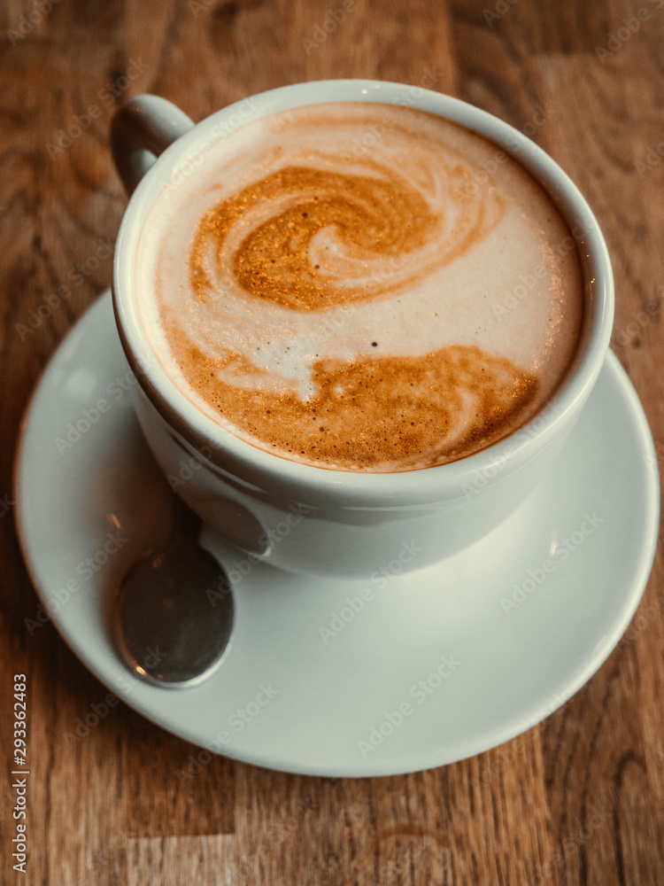 A beautiful cup of cappuccino with latte art in the wooden background. Minimal composition. Copy space for your text. A beautiful cup of cappuccino with latte art in the wooden background. Minimal composition. Copy space for your text.