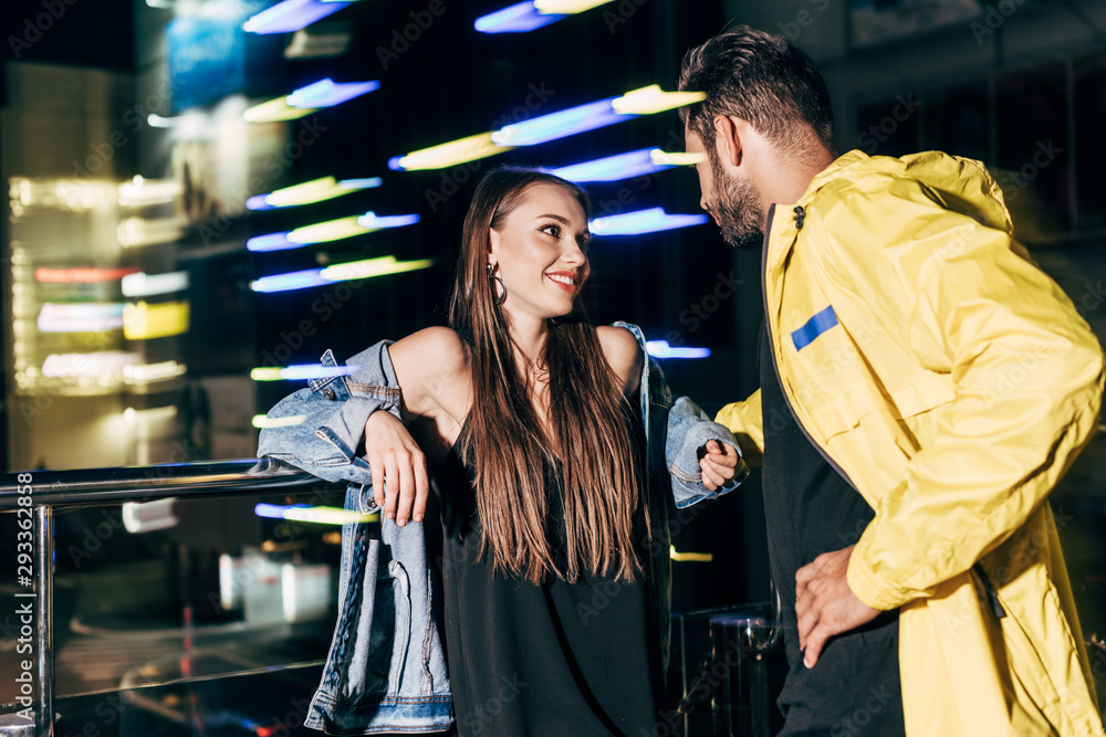 Obraz premium smiling girlfriend and boyfriend talking and looking at each other in night city