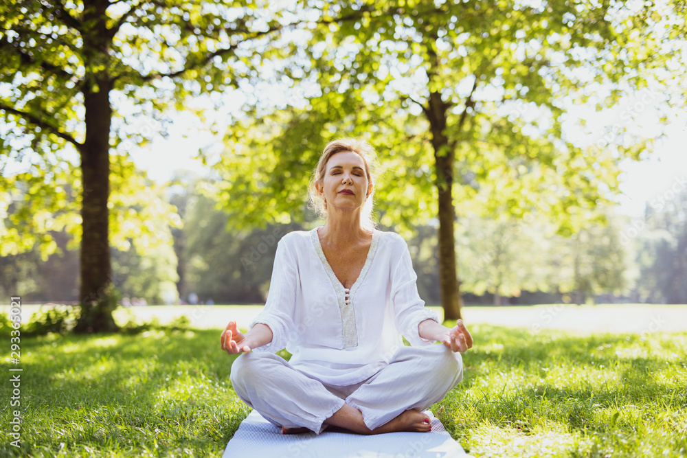 Eine attraktive Best-Ager Frau macht Meditations-Übungen im Park Eine attraktive Best-Ager Frau macht Meditations-Übungen im Park