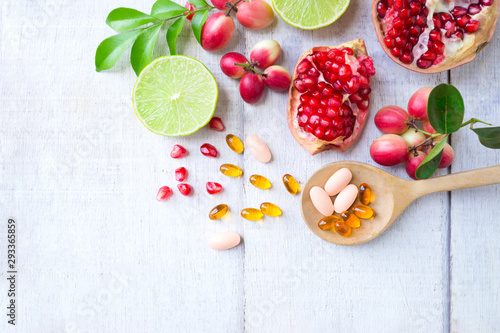 Vitamin supplements on wooden spoon with healthy fruits berry, lime, pomegranete on white wooden background.Top view. photo