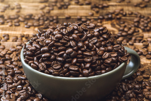 Cup full of Black coffee grains lie on a brown wooden table, background image. Coffee beans in a green cup.