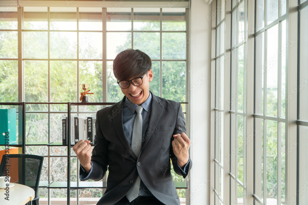 Young Asian businessman excited happy and celebrating success in the workplace after see finalizing the annual sales report. Concept of new entrepreneur successful Young Asian businessman excited happy and celebrating success in the workplace after see finalizing the annual sales report. Concept of new entrepreneur successful