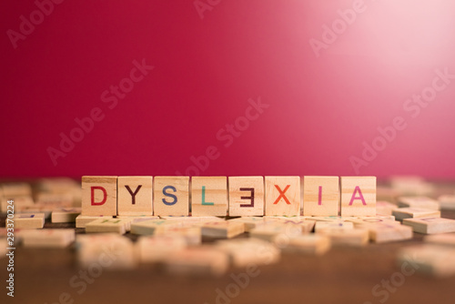wooden alphabet blocks with DYSLEXIA word in the center on wooden table against pink background. Concept of Dyslexia awareness and human brain development photo