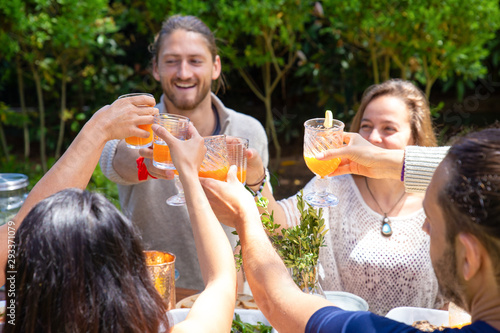 Cheerful friends clinking glasses outdoor. Happy young friends holding glasses with refreshing beverages and spending time together in backyard. Celebrating concept