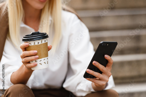 Cropped image of young woman using cellphone and drinking coffee