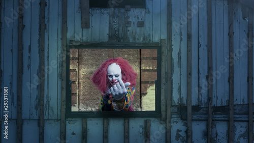 An evil clown looks out of a window and waves at you photo