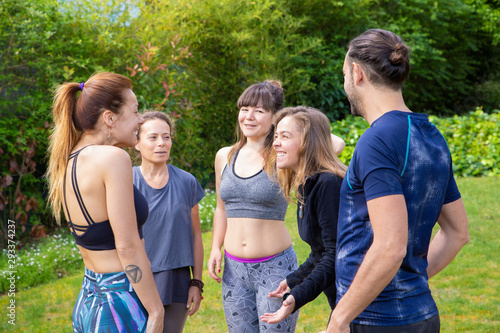 Cheerful young people in sportswear outdoor. Group of happy young man and women gathering together for yoga practice on green lawn. Yoga concept