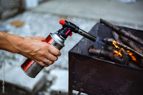 Lighter with pistol with gas cartridge. A girl lights the fire in the barbecue with wood.