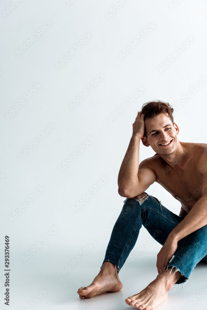positive and sexy man touching hair and sitting on white positive and sexy man touching hair and sitting on white