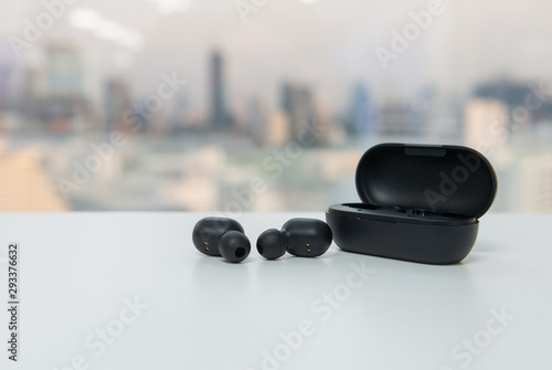 Fotografija True wireless earbuds with battery case on the white table with blur city scape