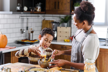 Son is helping mother to prepare pumpkin pie. American family. Single mother. Household chores for kids.