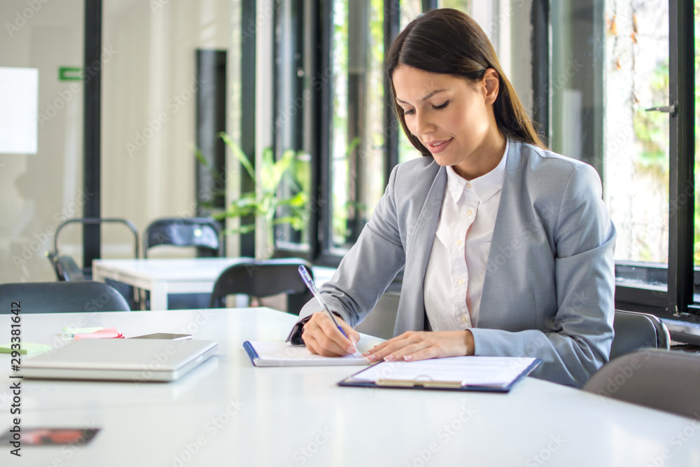 Self employed female entrepreneur taking notes while working with papers in office Self employed female entrepreneur taking notes while working with papers in office