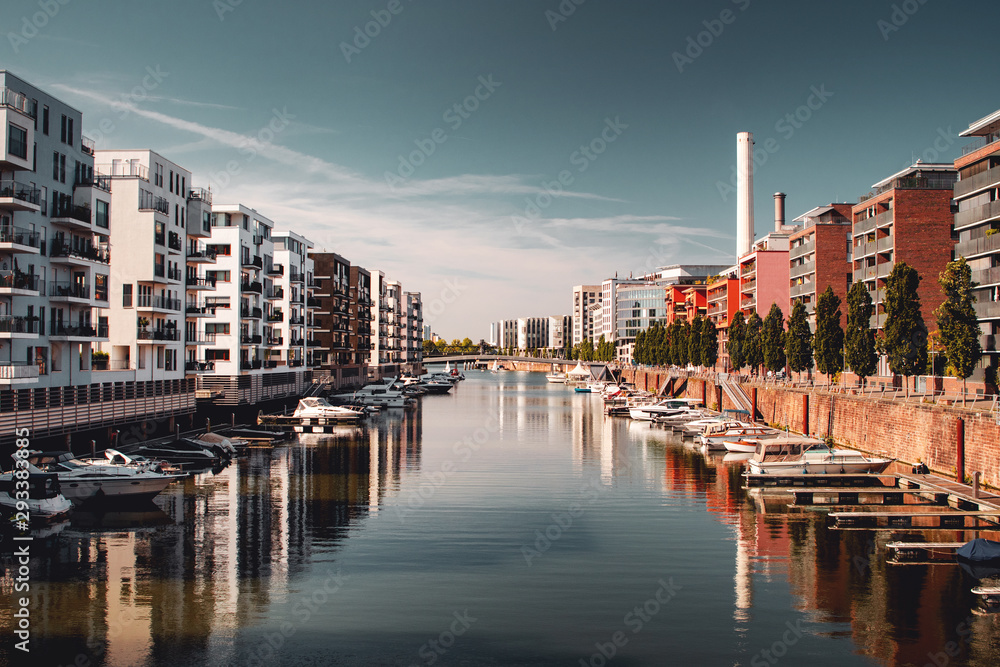 Modern luxury home buildings at the riverside with a marina view with small boats on a bright sunny blue sky day. Water view from the flat. Marina Westhafen, Frankfurt am Main, Germany
