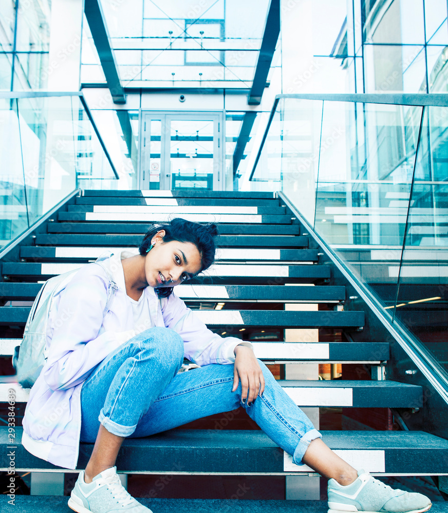 young cute indian girl at university building sitting on stairs reading a book, wearing hipster glasses, lifestyle people concept