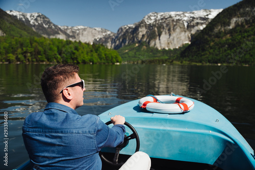 Handsome young guy controls a motorboat on a mountain lake