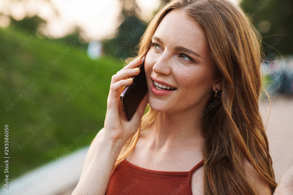 Ginger woman walking in park talking by mobile phone. Ginger woman walking in park talking by mobile phone.