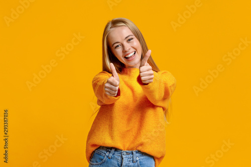 Joyful teenage girl showing thumbs up on orange background photo