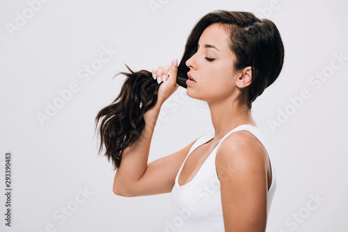 side view of brunette beautiful woman holding long healthy and shiny hair isolated on grey