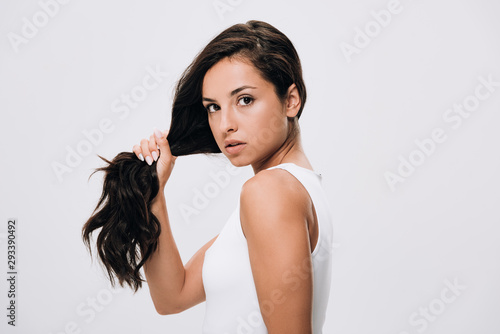 brunette beautiful woman holding long healthy and shiny hair isolated on grey