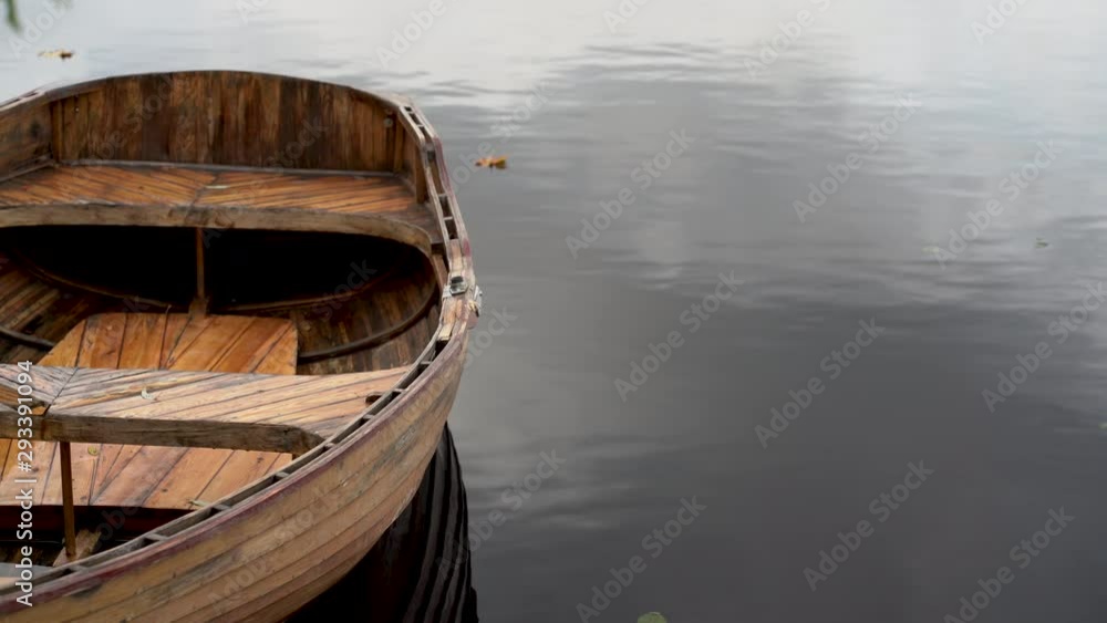 A wooden boat without oars is tied at the pier with a tree and sways in the waves. Vidzeme, Latvia A wooden boat without oars is tied at the pier with a tree and sways in the waves. Vidzeme, Latvia