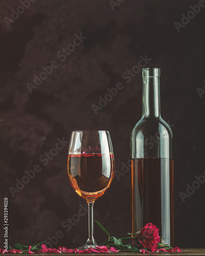 Bottle of rose wine and glass served with rose wine and rose petals, pink rose on dark background
