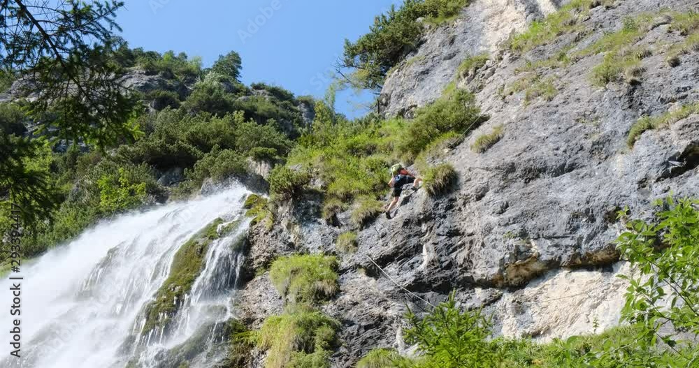 Female tourist climbing on Dalfazer waterfall via ferrata route near Achensee lake, Austria, on a sunny Summer day. Female tourist climbing on Dalfazer waterfall via ferrata route near Achensee lake, Austria, on a sunny Summer day.