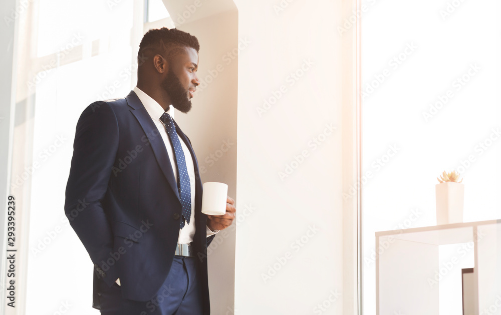 Handsome african businessman drinking coffee near window in office Handsome african businessman drinking coffee near window in office