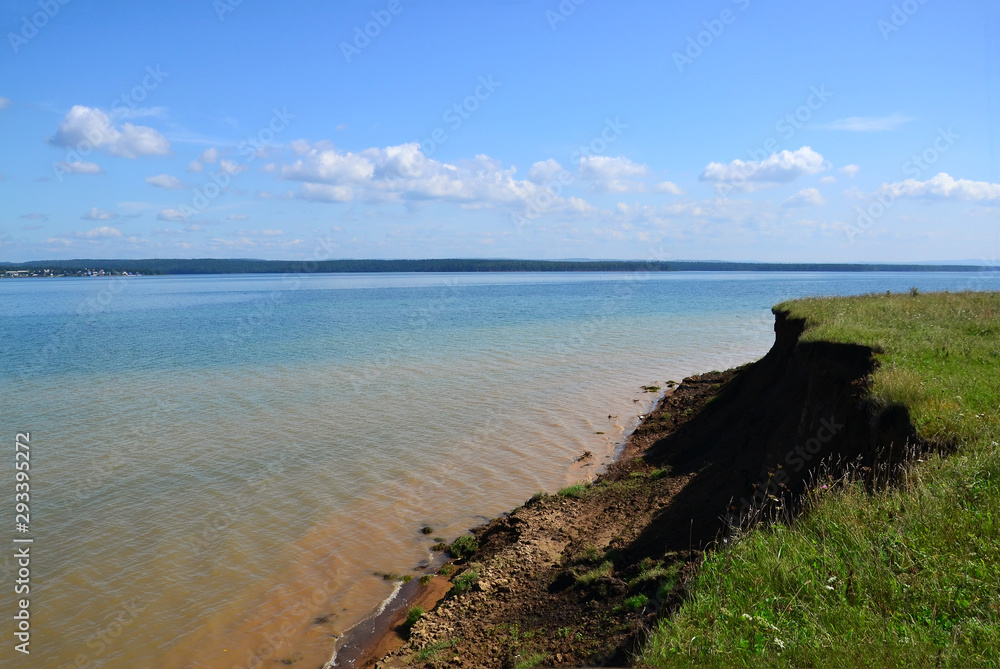 Coastline. Clouds float over the Bay. The shore is indented by water. The water is yellow near the shore of the sand.