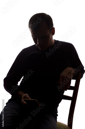 Young man sits with a mobile phone in hand - silhouette